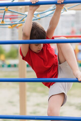 Fototapeta premium Happy boy playing and hanging on steel bar on playground. Children's exercises for health and concentration.
