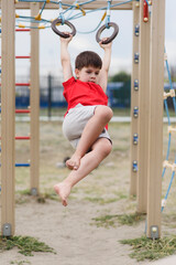 Obraz premium Happy boy playing and hanging on rings on playground. Kids exercises for health and concentration outdoors