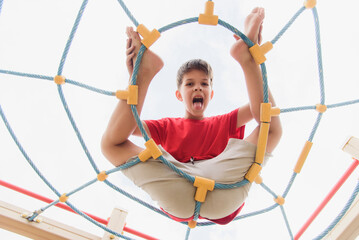 Happy boy playing and hanging on ropes on playground. Children's exercises for health and concentration