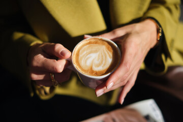 close-up hands holding a cup of coffee against the background of a street cafe with space for an inscription