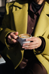 close-up hands holding a cup of coffee against the background of a street cafe with space for an inscription