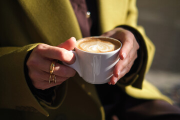close-up hands holding a cup of coffee against the background of a street cafe with space for an inscription