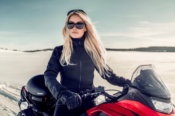 Confident woman riding a snowmobile in a snowy landscape on a bright winter day.