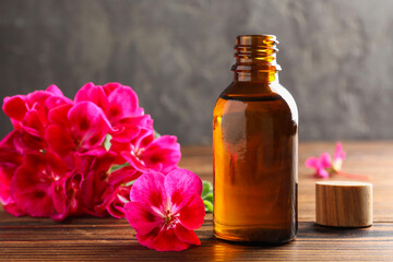 Geranium essential oil in bottle and beautiful flowers on wooden table