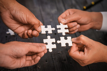 A group of people are putting together a jigsaw puzzle and trying to put the pieces together. This is a scene where everyone is working together on a wooden table, holding a jigsaw puzzle.