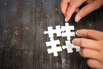 A group of people are putting together a jigsaw puzzle and trying to put the pieces together. This is a scene where everyone is working together on a wooden table, holding a jigsaw puzzle.