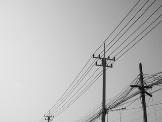 Black and white photo of Reinforced concrete pillar with high-voltage wires against a clear sky....