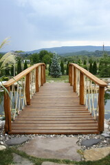 Obraz premium Beautiful wooden bridge over a pond, with plants and stones, on a sunny day.