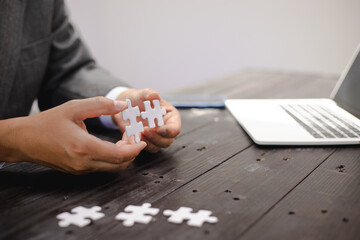 Businessman sitting at a table intently completing a jigsaw puzzle, demonstrating problem-solving,...