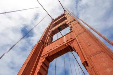 A stunning view of the Golden Gate Bridge tower against a backdrop of blue sky and clouds,...