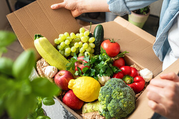 Ripe farm grown fruits and vegetables in cardboard box. Woman unpacking her online order of organic and healthy vegetables.