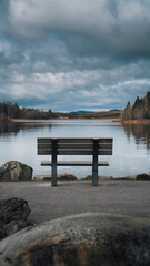 A solitary bench overlooking a tranquil lake with a cloudy sky, evoking a sense of serenity and peace. 
