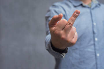 Man in a shirt showing a crude fuck gesture, middle finger sign, close-up against a concrete wall.