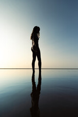 silhouette of young slim woman wearing bikini on the beach at sunset