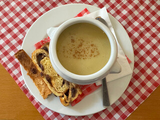 Creamy soup with cinnamon and pastry on checkered tablecloth