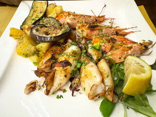 Grilled seafood and vegetables with lemon garnish on a white plate