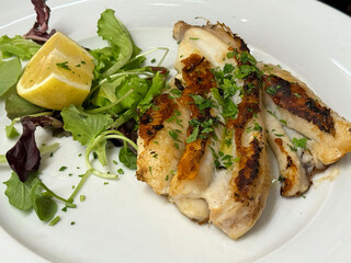 Grilled fish fillet with lemon and fresh herbs on a white plate