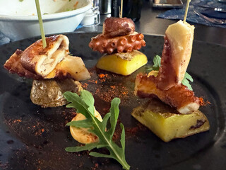 Gourmet octopus tapas on black plate with arugula and potatoes