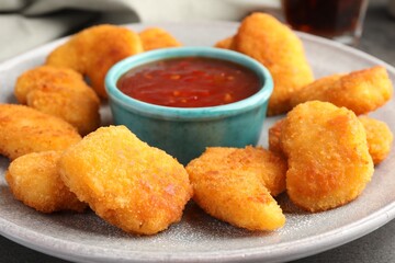 Plate with hot chili sauce and nuggets on grey table, closeup