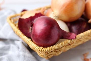 Wicker basket with fresh onions and peels on white table, closeup