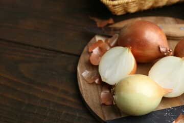 Fresh onions with peels on wooden table, closeup. Space for text