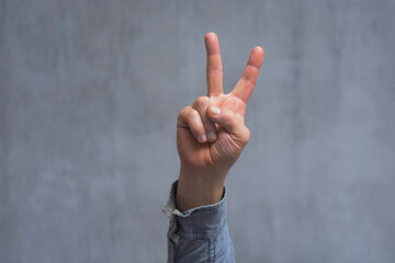 Man in a shirt showing gesture V means victory, peace sign or protest sign, close-up against a...