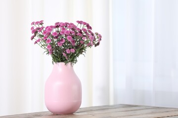 Beautiful pink flowers in vase on wooden table indoors. Space for text