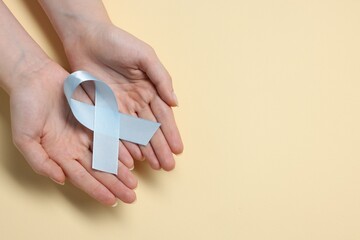 Woman with light blue ribbon on beige background, top view and space for text. Childhood cancer...