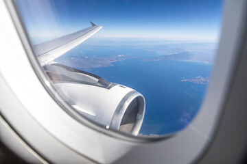 airplane's engine and wing are visible from a window over the Greek Aegean coast
