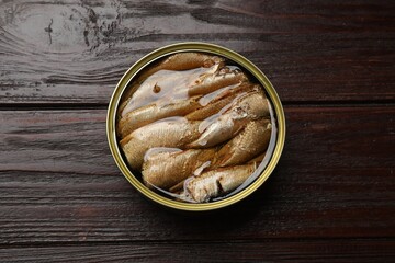 Tasty sprats in tin can on wooden table, top view