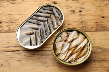 Tasty sprats in tin cans on wooden table, flat lay