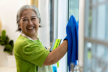 Asian housekeeper Senior Woman Cleaning glass Window with nano cloth