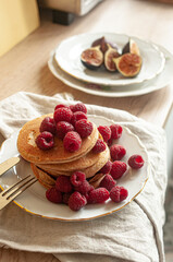 Delicious whole wheat healthy pancakes with raspberry, fork and knife styling natural light and copy space on the table with linen cloth background lifestyle