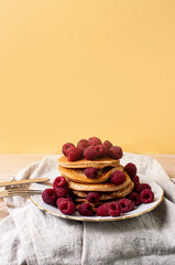 Delicious whole wheat healthy pancakes with raspberry, fork and knife styling natural light and copy space on the table with linen cloth background lifestyle