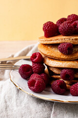 Delicious whole wheat healthy pancakes with raspberry, fork and knife styling natural light and copy space on the table with linen cloth background lifestyle