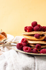 Delicious whole wheat healthy pancakes with raspberry, fork and knife styling natural light and copy space on the table with linen cloth background lifestyle