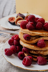 Delicious whole wheat healthy pancakes with raspberry, fork and knife styling natural light and copy space on the table with linen cloth background lifestyle