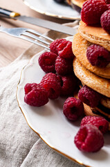 Delicious whole wheat healthy pancakes with raspberry, fork and knife styling natural light and copy space on the table with linen cloth background lifestyle
