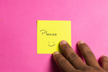 A hand is touching a yellow sticky note that says please