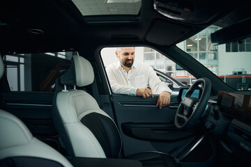 Portrait of cheerful adult Caucasian man examining auto at showroom store