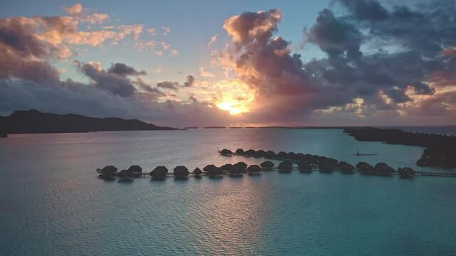 Overwater bungalows in Bora Bora colorful sunset, warm glow on turquoise water, dramatic colorful clouds sky background. Popular tourist destination. Remote wild nature paradise, exotic summer travel