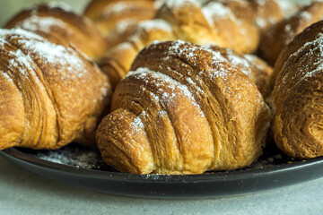 Plate of homemade croissants dusted with powdered sugar. Blurred background