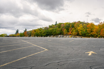 Empty parking lot bordered by autumnal trees on the top of a mountain on a cloudy day