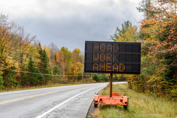 Digital road sign indicating roadworks ahead on a trailer along a forest road in the mountains on a cloudy autumn day