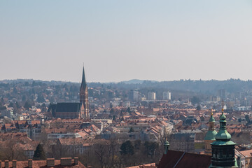 Fototapeta premium Scenic aerial view of Graz seen from Schlossberg, Styria, Austria, Europe. Unesco world heritage site with red-roofed buildings. Majestic church Herz Jesu Kirche in distance. Vibrant cityscape scene
