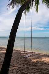 Rustic wooden swing hanging from exotic palm tree extending over pristine sand beach on Phu Quoc island, Vietnam, South East Asia. Relaxing scene on tropical island. Turquoise sea of Thailand Gulf