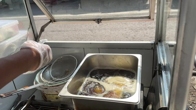 Street food vendor frying food in hot oil at a small cart