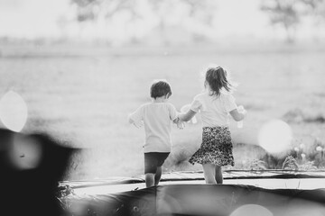 Young children lovingly play together on a trampoline in their parents' garden with a view from the living room