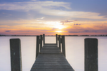 Obraz premium Cloudscape sky with jetty and flat horizon with trees reflecting in the tranquil lake during sunrise.