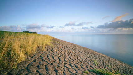 Massive dike along the waterfront of the Dutch coastline that curves away in a bend towards the horizon